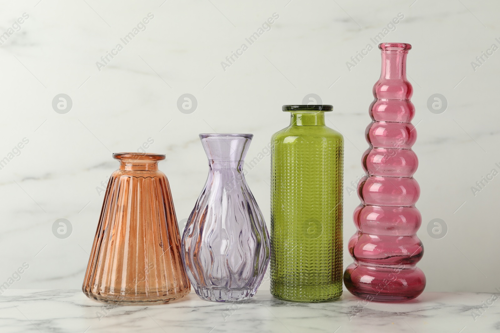 Photo of Different beautiful glass vases on white marble table