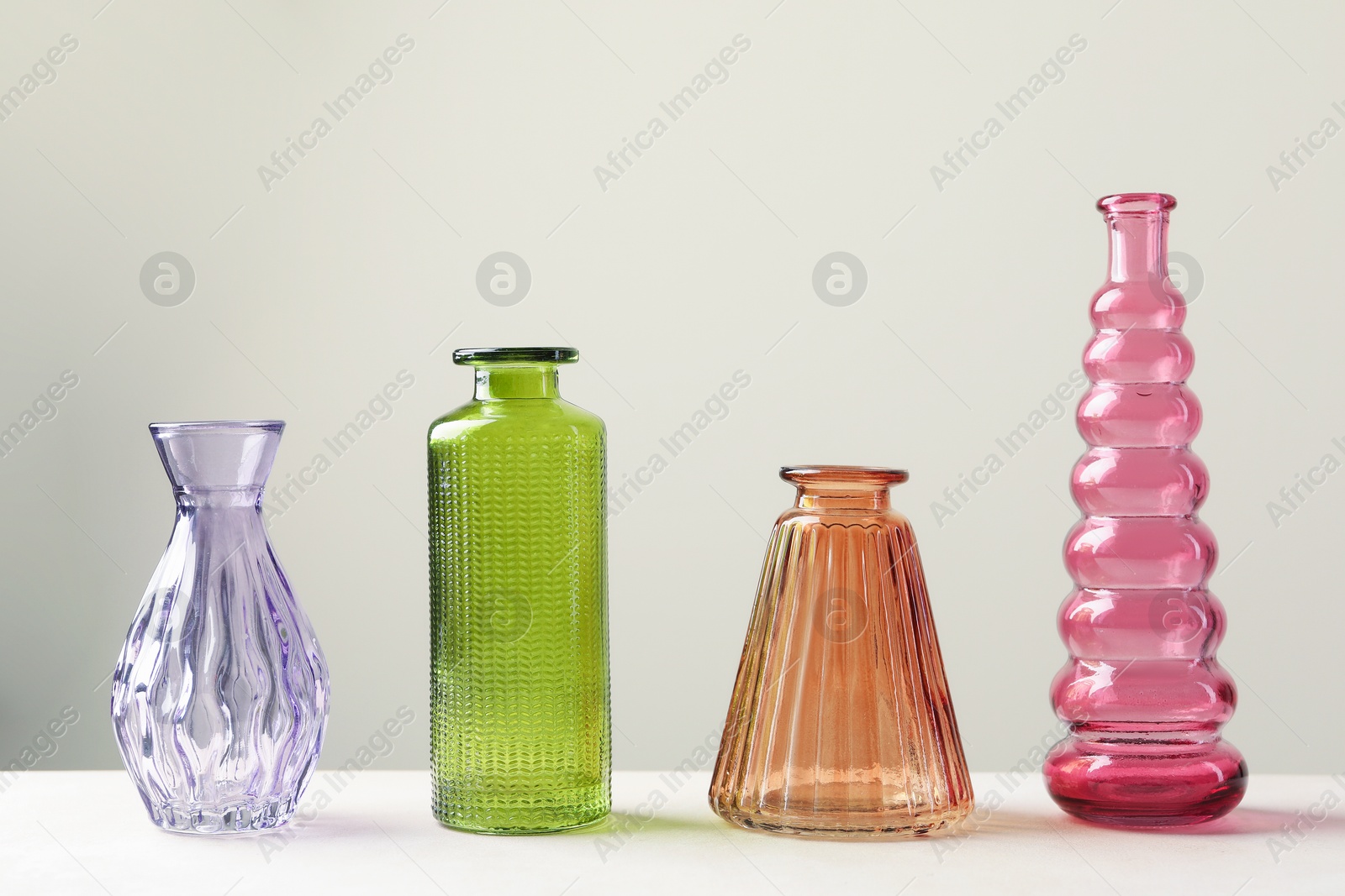 Different beautiful glass vases on white table against light grey background Photo of Different beautiful glass vases on white table against light grey background