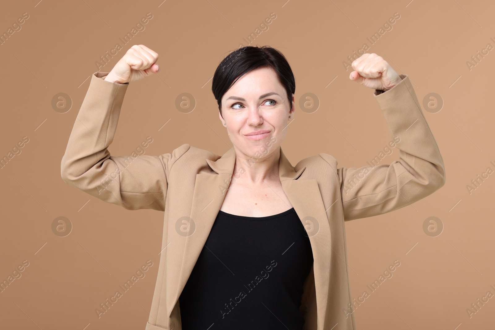 Photo of Strength. Beautiful businesswoman in suit showing her biceps on beige background