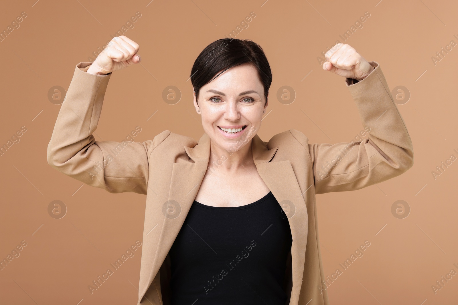 Photo of Strength. Smiling businesswoman in suit showing her biceps on beige background