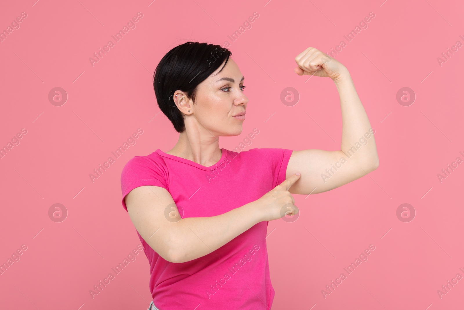 Photo of Strength. Beautiful woman showing her biceps on pink background