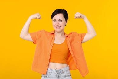 Photo of Strength. Smiling woman showing her biceps on yellow background