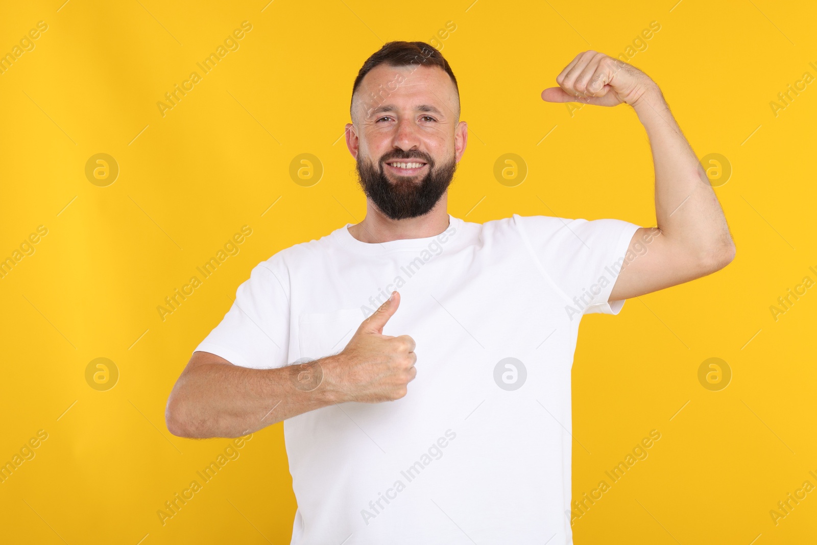 Photo of Strength. Smiling man showing his biceps and thumbs up on yellow background