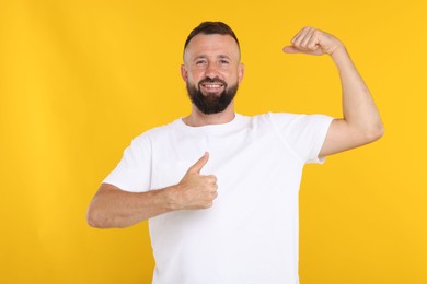 Photo of Strength. Smiling man showing his biceps and thumbs up on yellow background