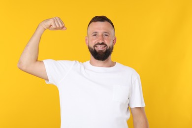 Photo of Strength. Smiling man showing his biceps on yellow background