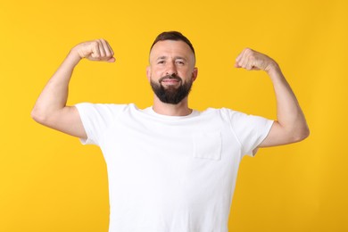 Photo of Strength. Handsome man showing his biceps on yellow background