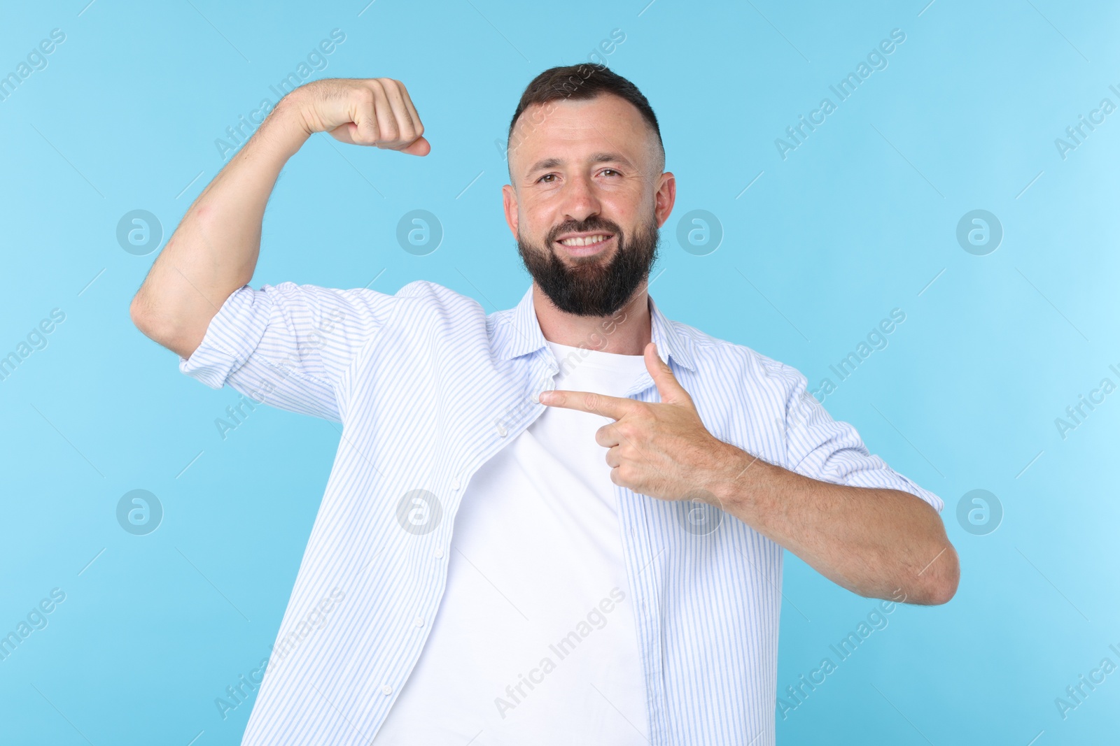 Photo of Strength. Smiling man pointing at his biceps on light blue background