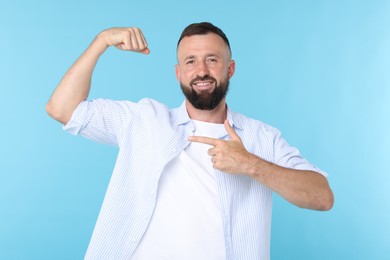 Photo of Strength. Smiling man pointing at his biceps on light blue background