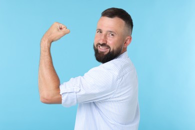 Photo of Strength. Smiling man showing his biceps on light blue background