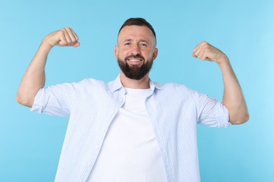 Photo of Strength. Smiling man showing his biceps on light blue background