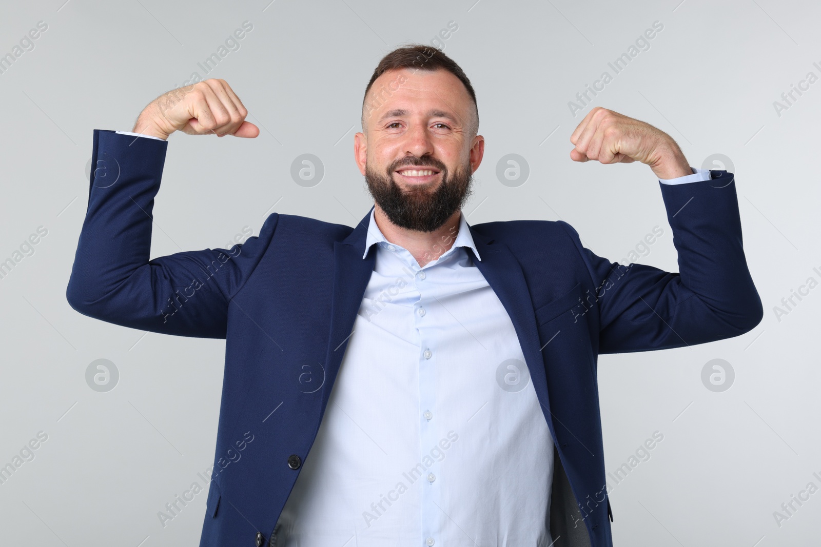 Photo of Strength. Smiling man in suit showing his biceps on grey background