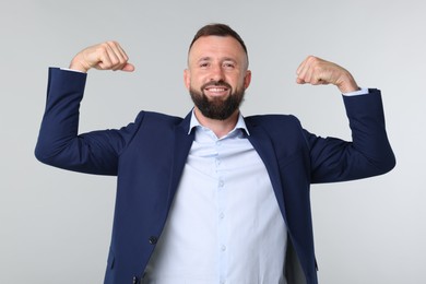 Photo of Strength. Smiling man in suit showing his biceps on grey background