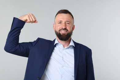 Photo of Strength. Smiling man in suit showing his biceps on grey background