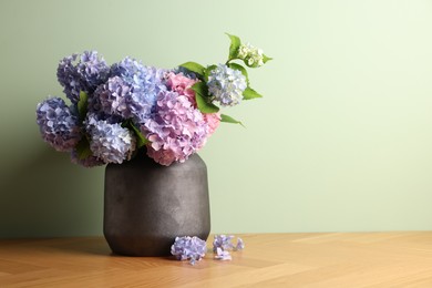 Photo of Beautiful hortensia flowers in vase on wooden table near light green wall. Space for text