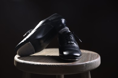 Photo of Pair of shoes for tap dance on wooden stool against black background, closeup
