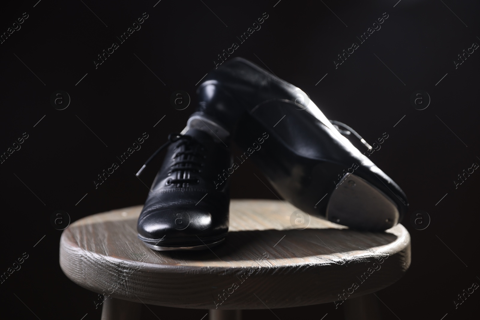 Photo of Pair of shoes for tap dance on wooden stool against black background, closeup