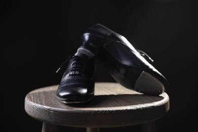 Photo of Pair of shoes for tap dance on wooden stool against black background, closeup
