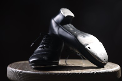 Photo of Pair of shoes for tap dance on wooden stool against black background, closeup
