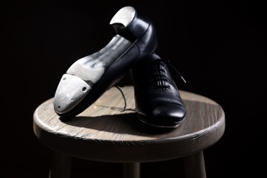 Photo of Pair of shoes for tap dance on wooden stool against black background, closeup
