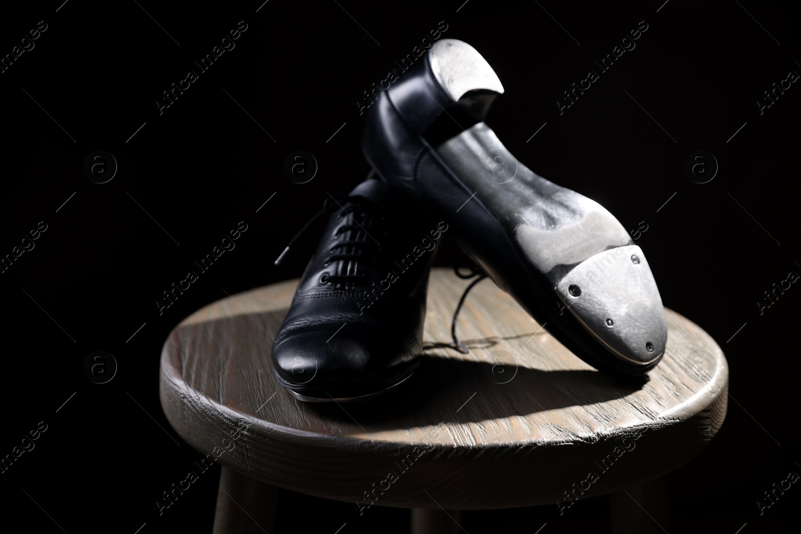 Photo of Pair of shoes for tap dance on wooden stool against black background, closeup