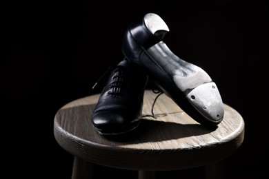 Photo of Pair of shoes for tap dance on wooden stool against black background, closeup
