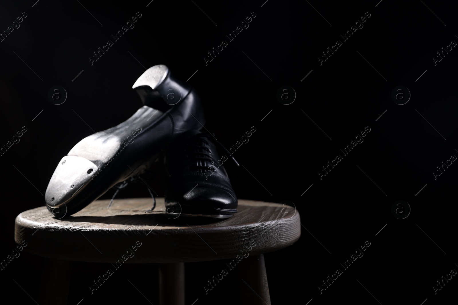 Photo of Pair of shoes for tap dance on wooden stool against black background, closeup. Space for text