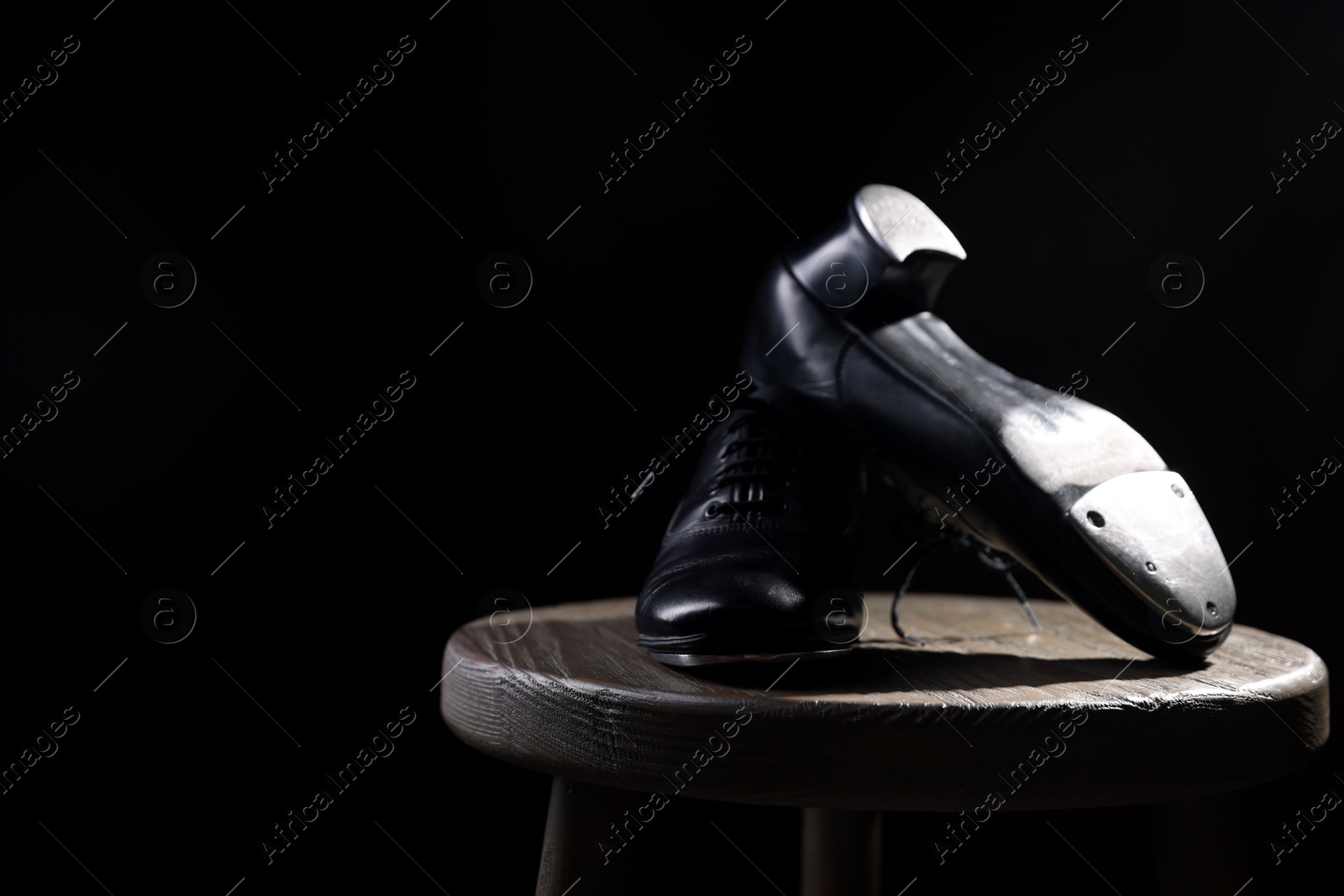 Photo of Pair of shoes for tap dance on wooden stool against black background, closeup. Space for text