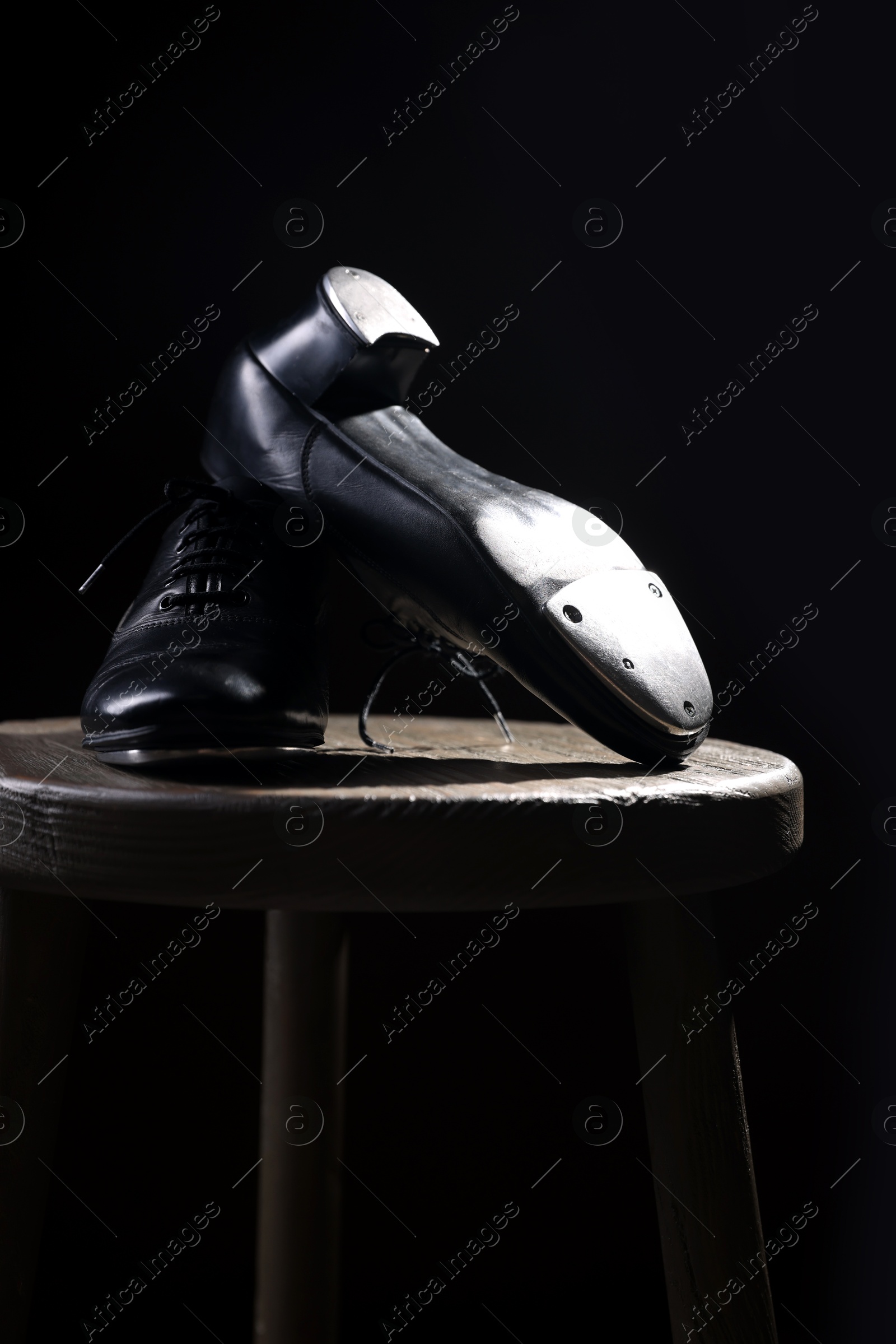 Photo of Pair of shoes for tap dance on wooden stool against black background, closeup