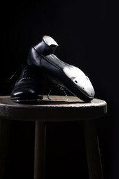 Photo of Pair of shoes for tap dance on wooden stool against black background, closeup