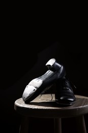 Photo of Pair of shoes for tap dance on wooden stool against black background, closeup