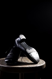 Photo of Pair of shoes for tap dance on wooden stool against black background, closeup