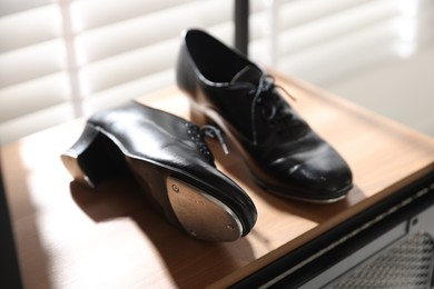 Photo of Pair of shoes for tap dance on wooden shelf indoors, closeup