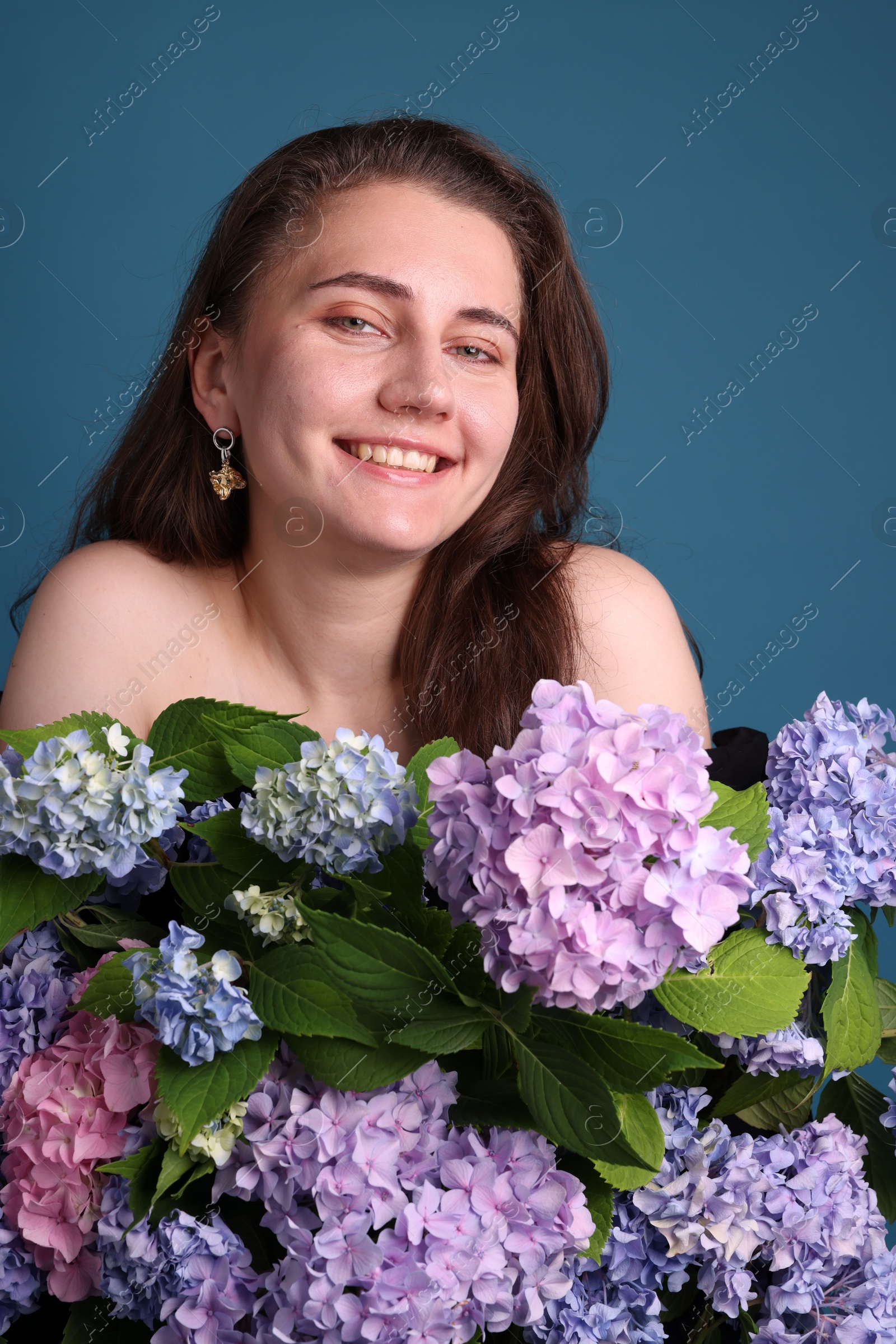 Photo of Portrait of smiling woman with hortensia flowers on blue background