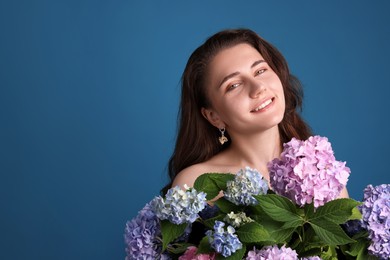 Photo of Portrait of smiling woman with hortensia flowers on blue background. Space for text