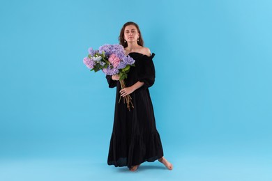 Photo of Beautiful woman in dress with hortensia flowers on light blue background