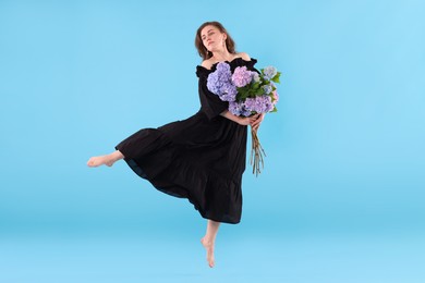 Photo of Beautiful woman in dress with hortensia flowers jumping on light blue background