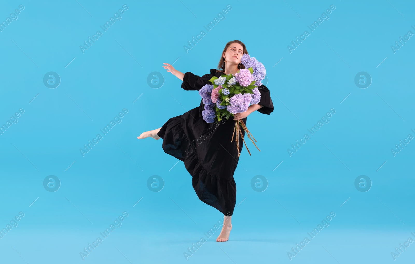 Beautiful woman in dress with hortensia flowers on light blue background Photo of Beautiful woman in dress with hortensia flowers on light blue background