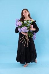 Photo of Beautiful woman in dress with bouquet of hortensia flowers on light blue background