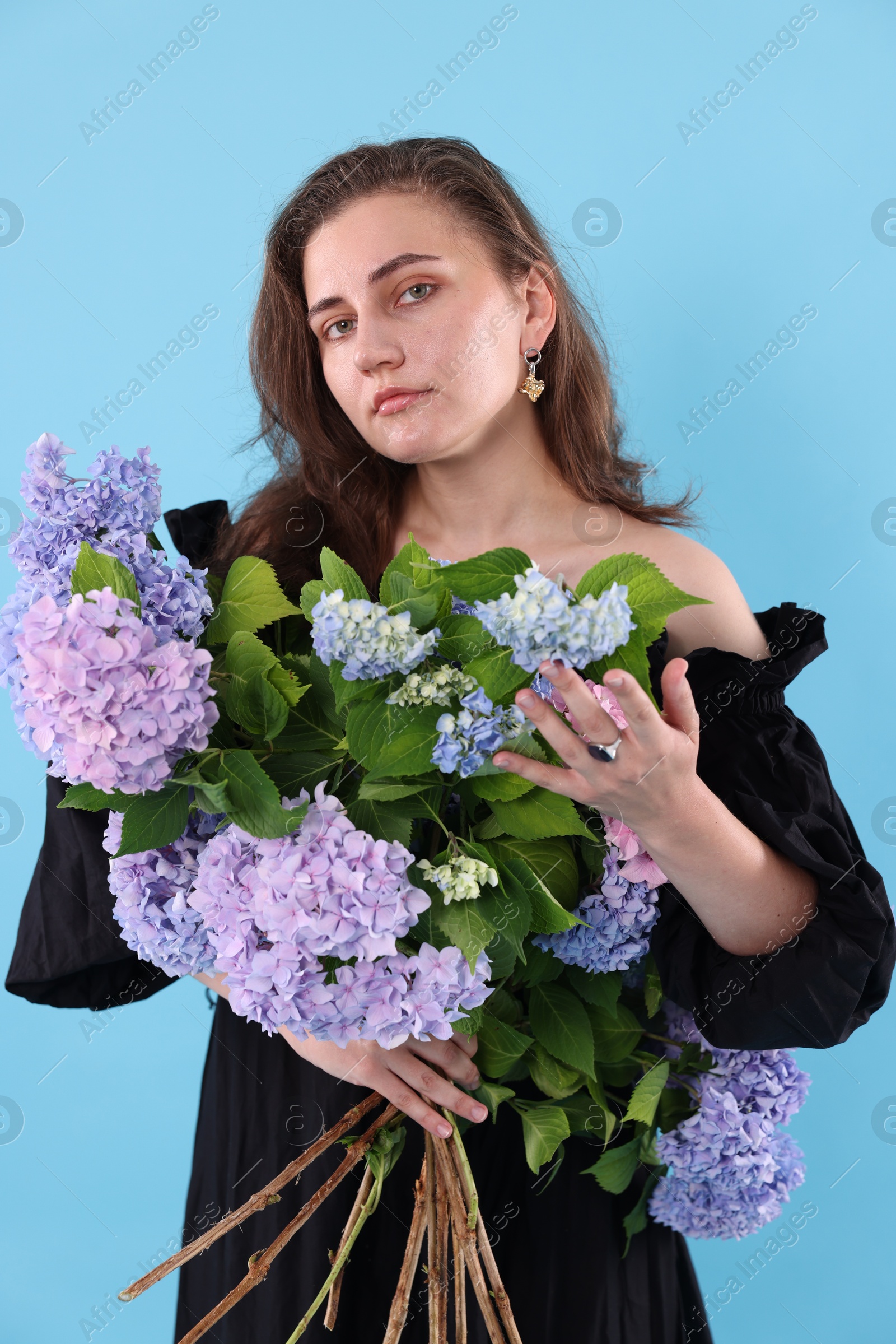 Photo of Portrait of beautiful woman with bouquet of hortensia flowers on light blue background