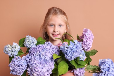 Photo of Portrait of smiling little girl with hortensia flowers on beige background