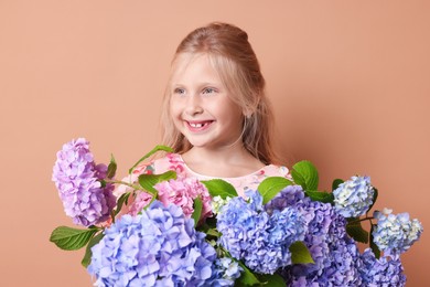 Photo of Smiling little girl with hortensia flowers on beige background