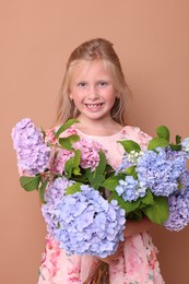 Photo of Portrait of smiling little girl with hortensia flowers on beige background