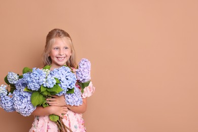 Photo of Smiling little girl with hortensia flowers on beige background. Space for text