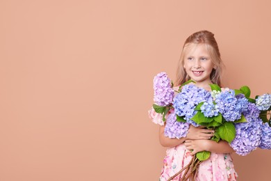 Photo of Smiling little girl with hortensia flowers on beige background. Space for text