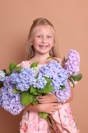 Photo of Portrait of smiling little girl with bouquet of hortensia flowers on beige background