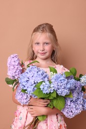 Photo of Portrait of beautiful little girl with bouquet of hortensia flowers on beige background