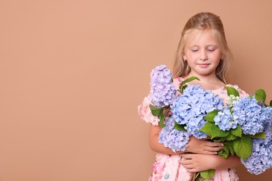 Photo of Beautiful little girl with bouquet of hortensia flowers on beige background. Space for text