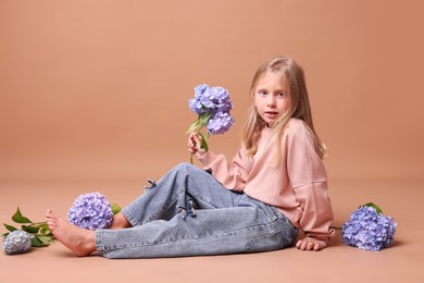 Photo of Beautiful little girl with hortensia flowers on beige background