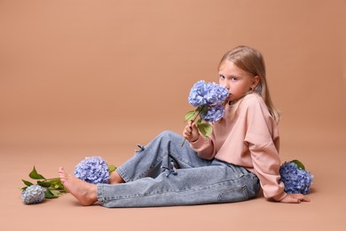 Photo of Beautiful little girl sniffing aromatic hortensia flowers on beige background