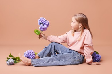 Photo of Beautiful little girl with hortensia flowers on beige background